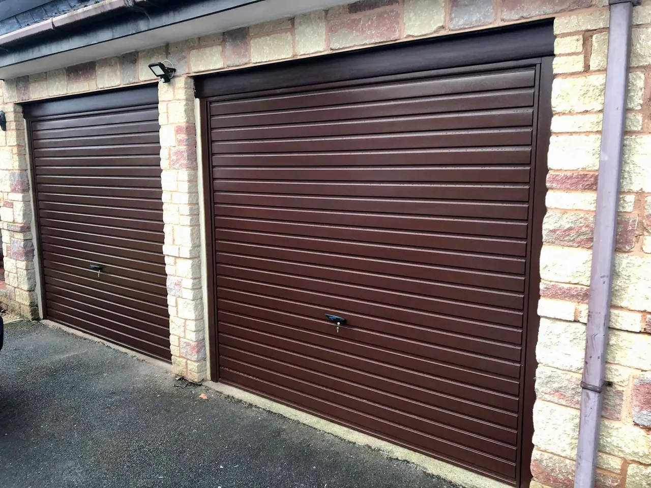 Brown up and over garage doors installed on a pair of brick-built residential garages.